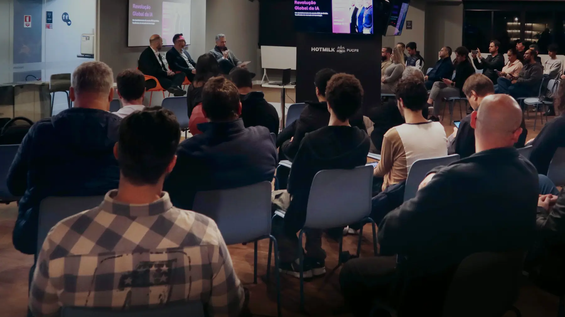 Plateia de executivos acompanhando uma palestra no auditório da HOTMILK PUCPR