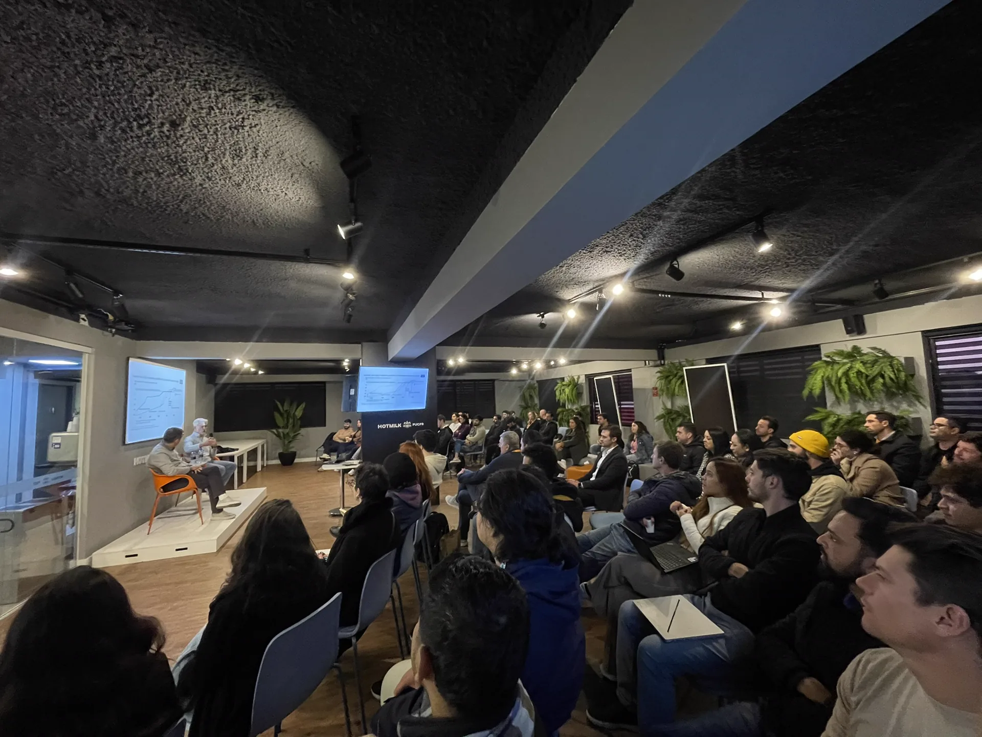 Plateia acompanha uma conversa com convidados no palco do Hub HOTMILK PUCPR