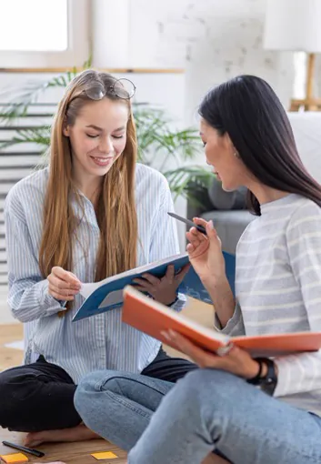Duas estudantes estudando juntas com livro e caderno