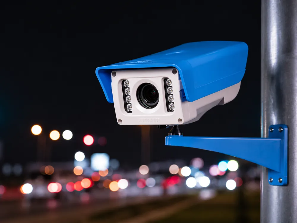Câmera de monitoramento veicular instalada em poste, com o trânsito ao fundo